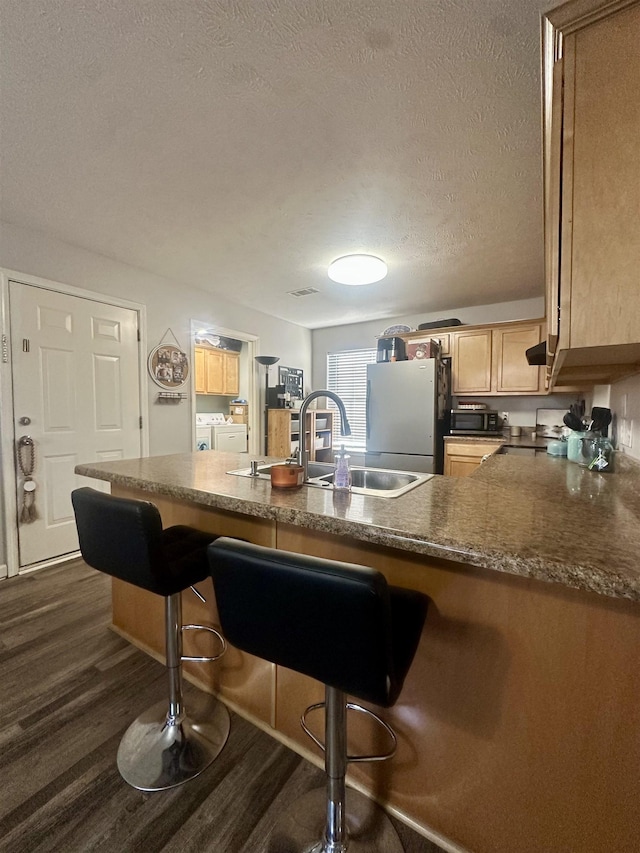 kitchen with a breakfast bar, washer and dryer, kitchen peninsula, and refrigerator