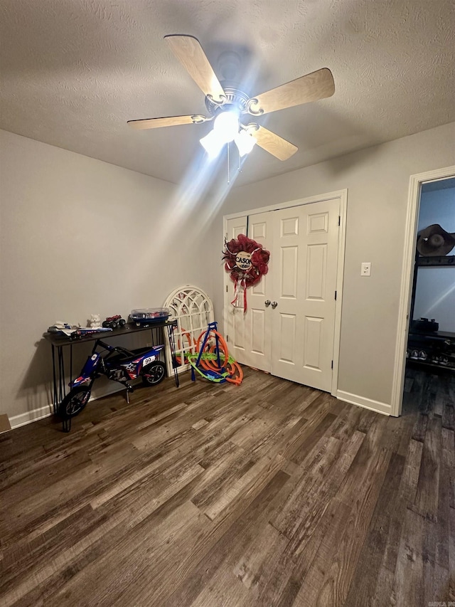 playroom featuring ceiling fan, dark hardwood / wood-style flooring, and a textured ceiling