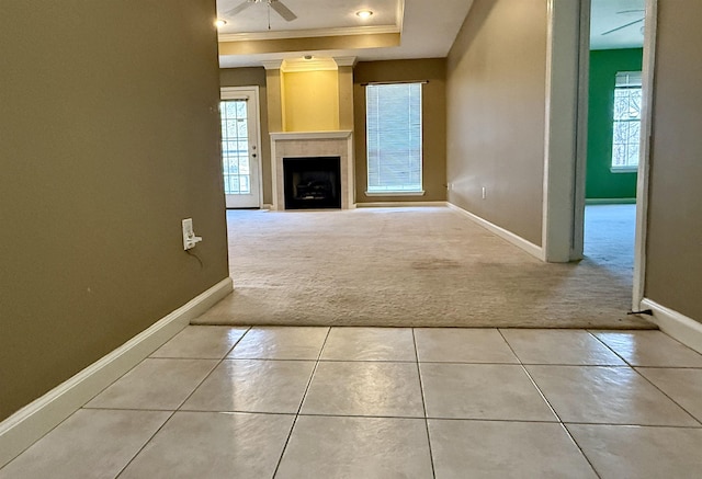 unfurnished living room featuring a tile fireplace, ornamental molding, a wealth of natural light, and a tray ceiling