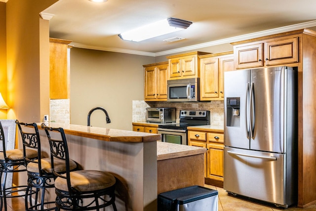 kitchen with appliances with stainless steel finishes, backsplash, a kitchen breakfast bar, ornamental molding, and kitchen peninsula