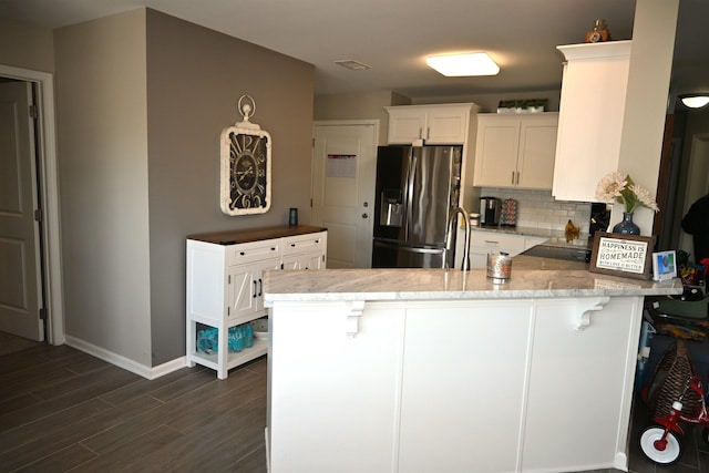 kitchen with a kitchen breakfast bar, stainless steel fridge, kitchen peninsula, and white cabinets