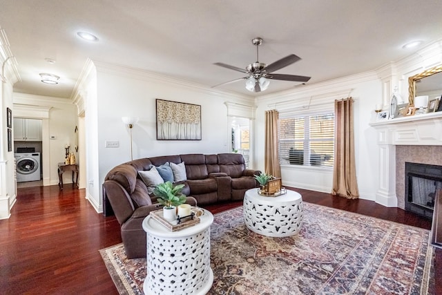 living room with washer / dryer, a tiled fireplace, ceiling fan, crown molding, and dark wood-type flooring