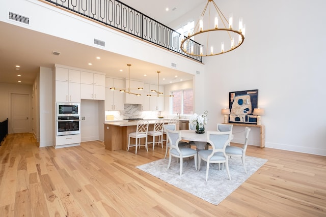 dining area featuring a chandelier, light hardwood / wood-style floors, and a high ceiling