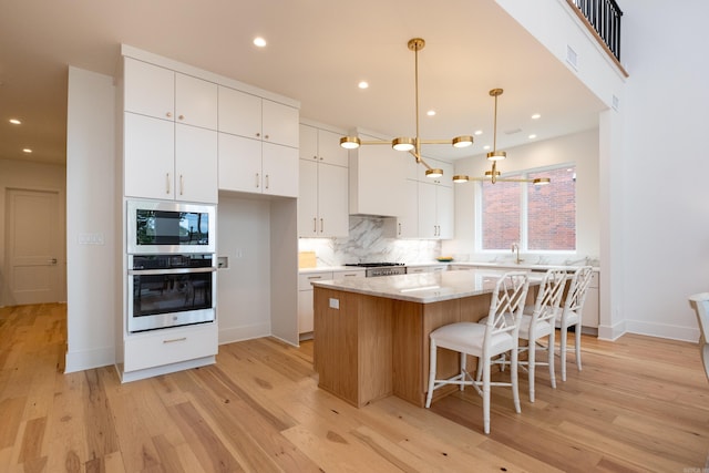 kitchen featuring white cabinetry, hanging light fixtures, a kitchen island, built in microwave, and oven