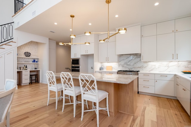 kitchen with white cabinetry, a center island, light hardwood / wood-style flooring, hanging light fixtures, and backsplash