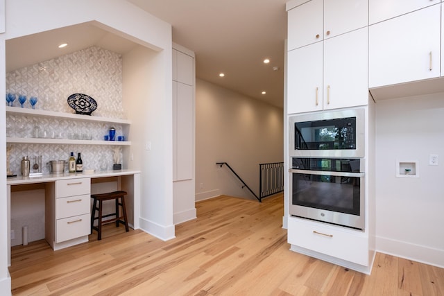 kitchen with tasteful backsplash, built in microwave, white cabinets, and light wood-type flooring