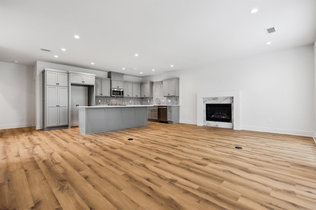 kitchen featuring gray cabinetry, tasteful backsplash, light wood-type flooring, a kitchen island, and stainless steel appliances