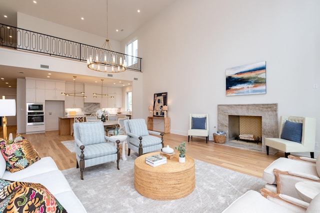 living room with a high ceiling, an inviting chandelier, a fireplace, and light hardwood / wood-style floors