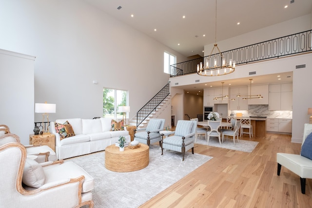 living room with an inviting chandelier, light hardwood / wood-style flooring, and a high ceiling