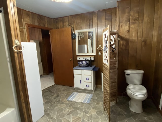 bathroom with vanity, a bathtub, toilet, and wood walls