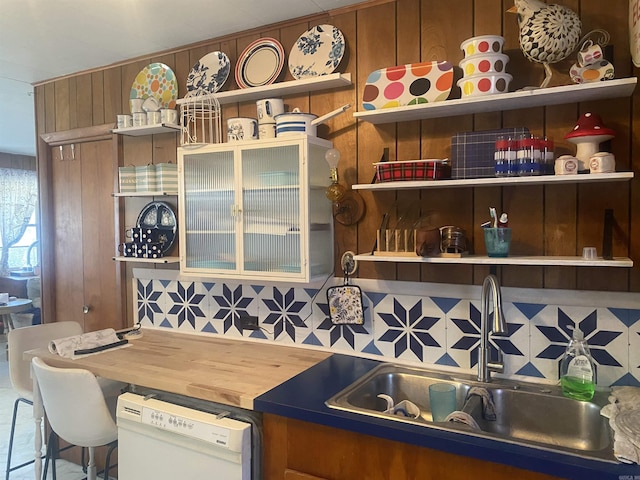 kitchen with wooden walls, dishwasher, sink, backsplash, and a kitchen bar