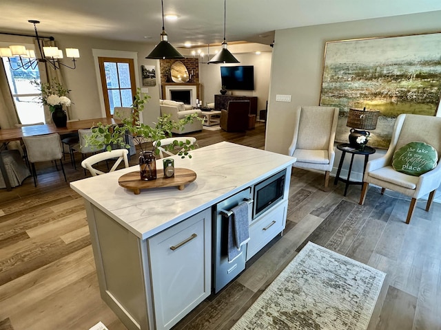 kitchen featuring a kitchen island, stainless steel microwave, white cabinetry, hanging light fixtures, and dark wood-type flooring