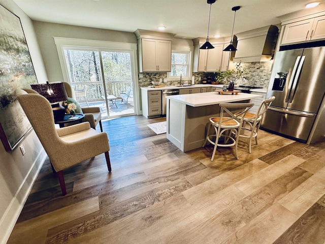 kitchen featuring sink, premium range hood, appliances with stainless steel finishes, light hardwood / wood-style floors, and decorative light fixtures