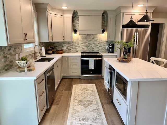 kitchen with sink, custom exhaust hood, tasteful backsplash, hanging light fixtures, and stainless steel appliances