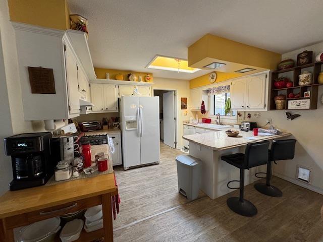 kitchen featuring sink, white appliances, a breakfast bar area, white cabinets, and kitchen peninsula