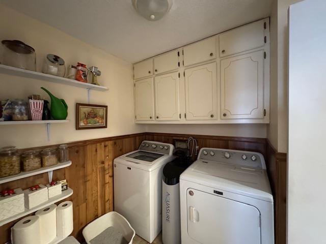 laundry room with cabinets, washing machine and dryer, and wood walls