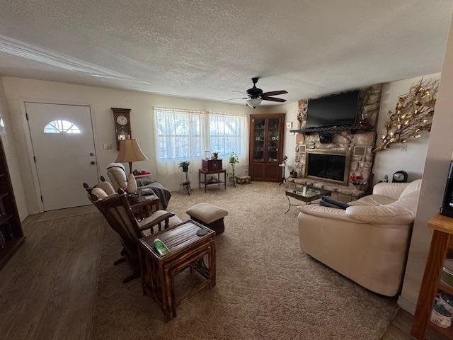 living room featuring ceiling fan, a fireplace, hardwood / wood-style floors, and a textured ceiling