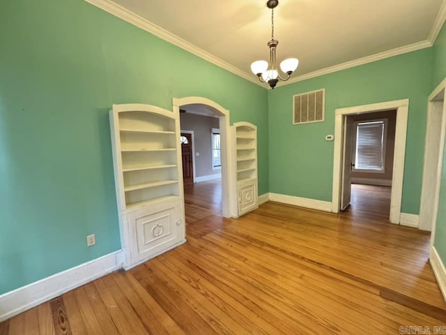 unfurnished dining area with wood-type flooring, built in features, ornamental molding, and a chandelier