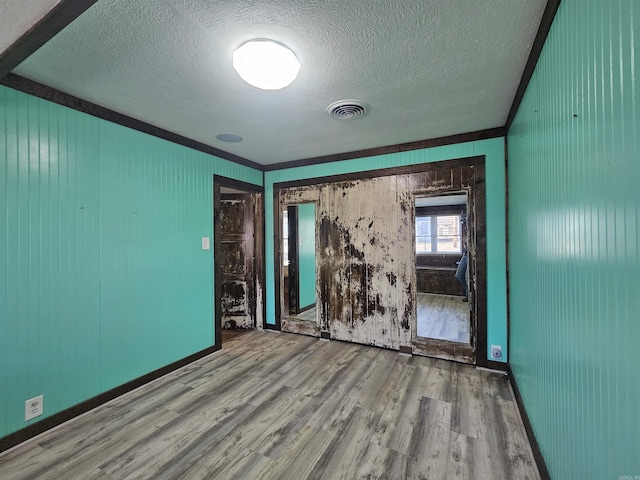 empty room with crown molding, a textured ceiling, and light wood-type flooring