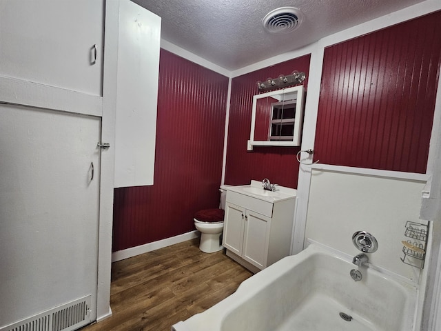 bathroom featuring a tub to relax in, toilet, a textured ceiling, vanity, and hardwood / wood-style floors