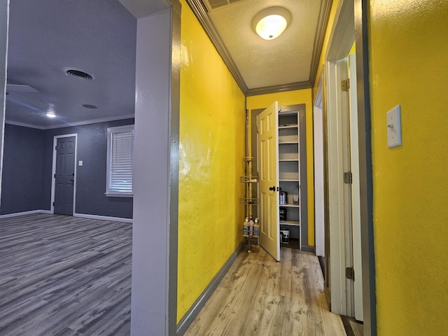 hall with ornamental molding, wood-type flooring, and a textured ceiling