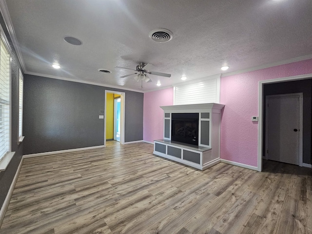 unfurnished living room with ceiling fan, a fireplace, wood-type flooring, ornamental molding, and a textured ceiling