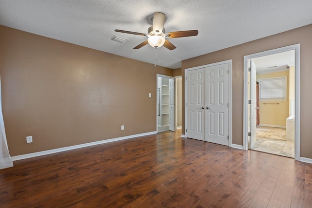 unfurnished bedroom featuring ensuite bathroom, dark wood-type flooring, a textured ceiling, and ceiling fan