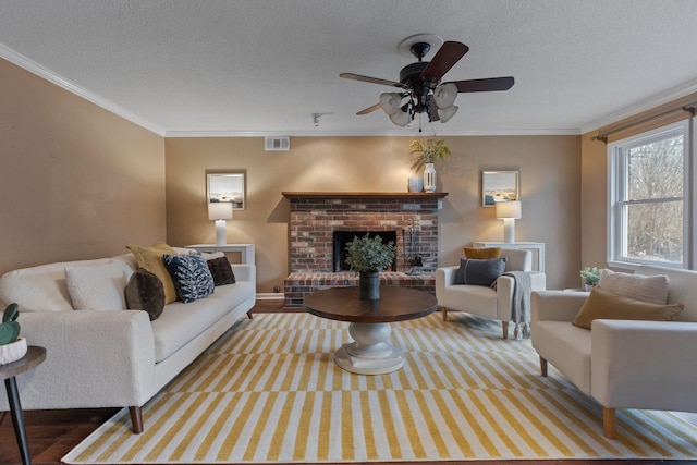 living room featuring crown molding, ceiling fan, a fireplace, light hardwood / wood-style floors, and a textured ceiling