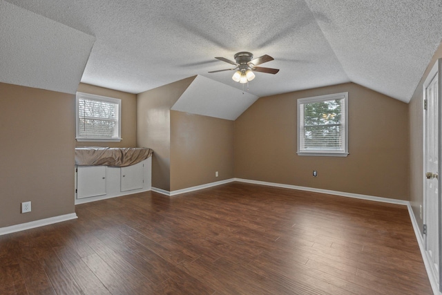 additional living space with ceiling fan, a healthy amount of sunlight, dark hardwood / wood-style floors, and vaulted ceiling