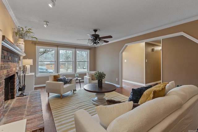 living room with crown molding, hardwood / wood-style flooring, ceiling fan, a fireplace, and a textured ceiling