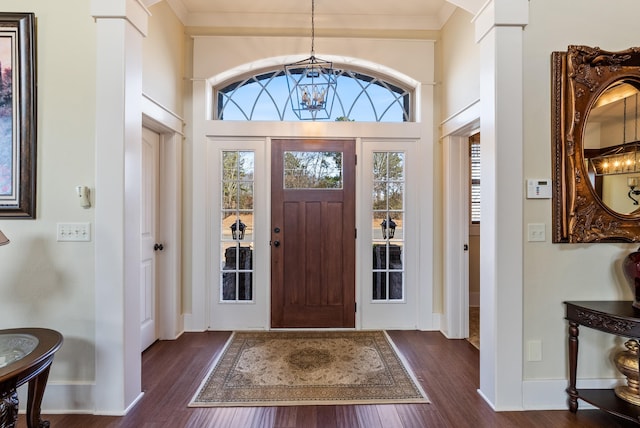 foyer with a notable chandelier, dark hardwood / wood-style floors, and ornate columns