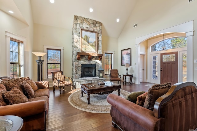 living room featuring dark wood-type flooring, a stone fireplace, high vaulted ceiling, and a wealth of natural light