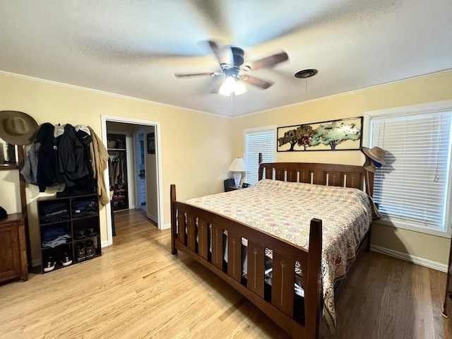 bedroom featuring crown molding, a spacious closet, ceiling fan, and light hardwood / wood-style flooring