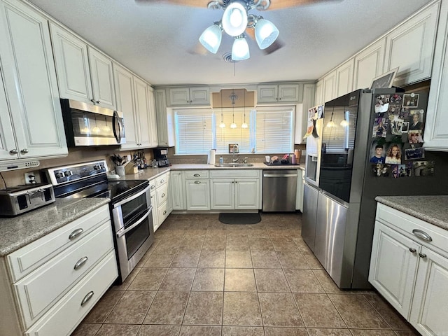 kitchen with light tile patterned flooring, sink, white cabinetry, ceiling fan, and stainless steel appliances