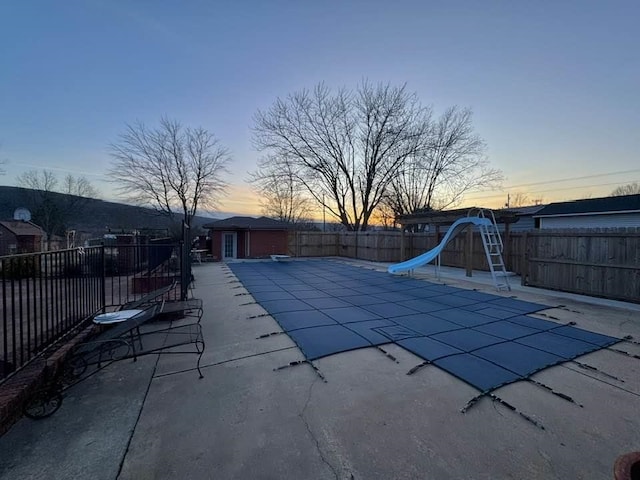 pool at dusk featuring a water slide and a patio