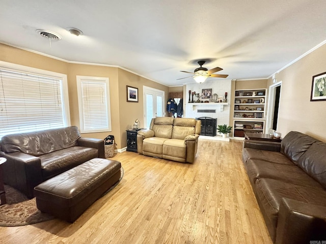 living room with built in features, ceiling fan, a fireplace, ornamental molding, and light hardwood / wood-style floors