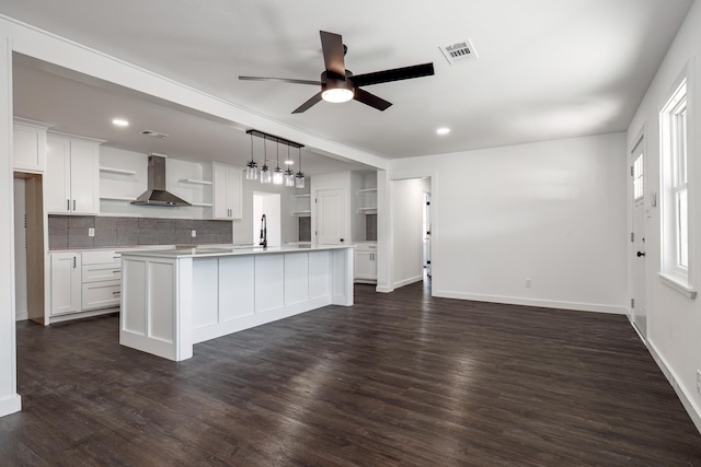 kitchen featuring white cabinets, an island with sink, hanging light fixtures, and wall chimney range hood