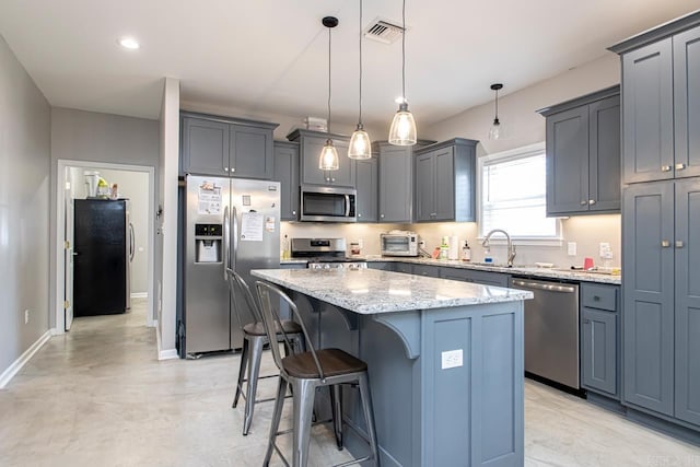 kitchen featuring sink, appliances with stainless steel finishes, a kitchen island, pendant lighting, and light stone countertops