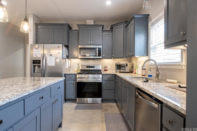 kitchen with light stone counters, hanging light fixtures, sink, and appliances with stainless steel finishes