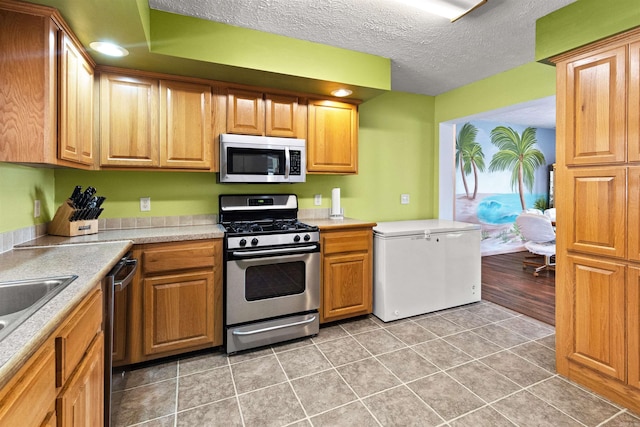 kitchen featuring stainless steel appliances, light tile patterned flooring, and a textured ceiling