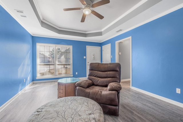 living area featuring hardwood / wood-style flooring, ornamental molding, a raised ceiling, and ceiling fan