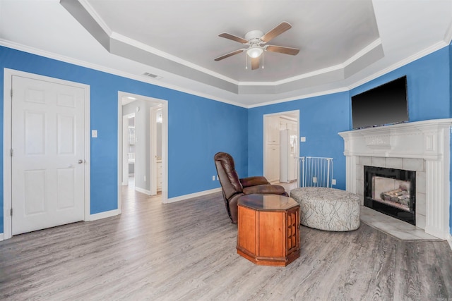 living room featuring a tile fireplace, wood-type flooring, ceiling fan, a tray ceiling, and crown molding