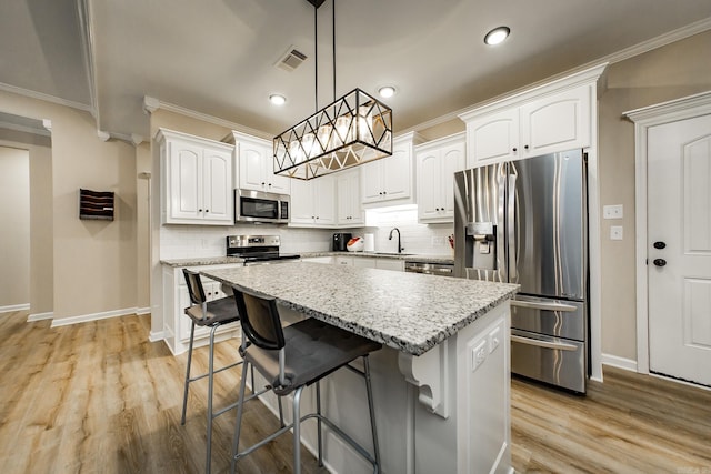 kitchen with a kitchen island, appliances with stainless steel finishes, pendant lighting, and white cabinets