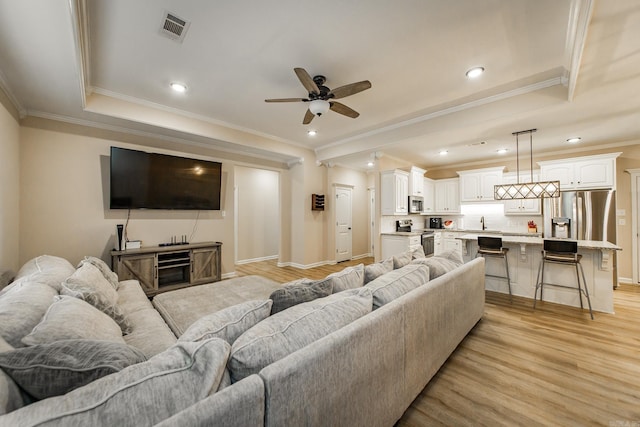 living room featuring a tray ceiling, ornamental molding, and light wood-type flooring