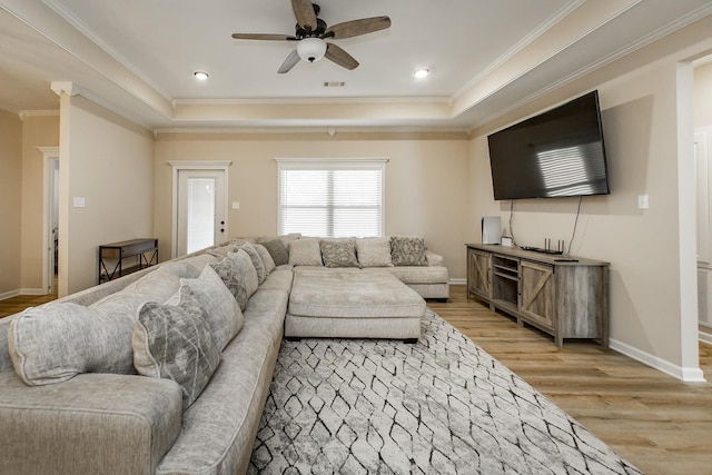 living room featuring crown molding, ceiling fan, a raised ceiling, and light wood-type flooring