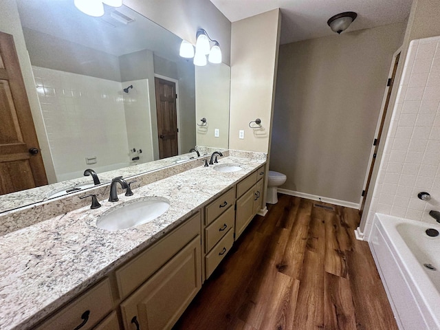 full bathroom with hardwood / wood-style flooring, tiled shower / bath, vanity, and toilet