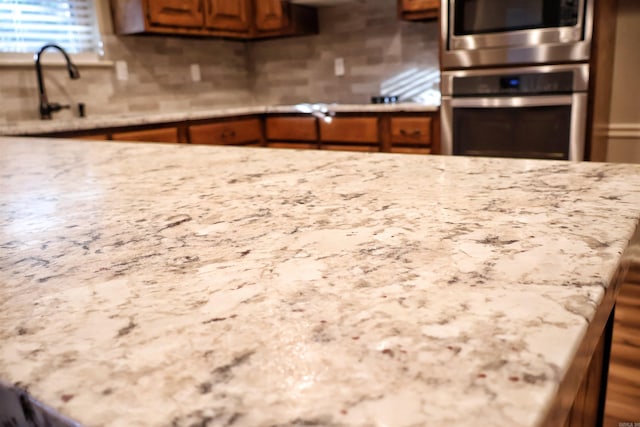 kitchen with tasteful backsplash, sink, light stone counters, and double oven