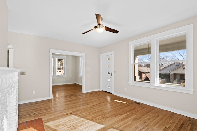 unfurnished room featuring ceiling fan, a tiled fireplace, and light hardwood / wood-style flooring