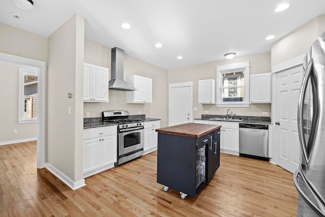 kitchen featuring a kitchen island, appliances with stainless steel finishes, butcher block counters, white cabinets, and wall chimney range hood