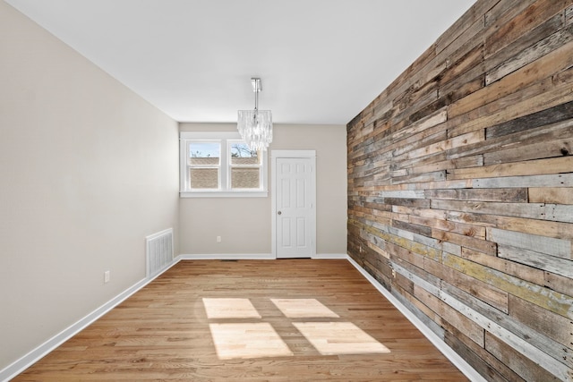 unfurnished dining area featuring a notable chandelier, light hardwood / wood-style floors, and wood walls